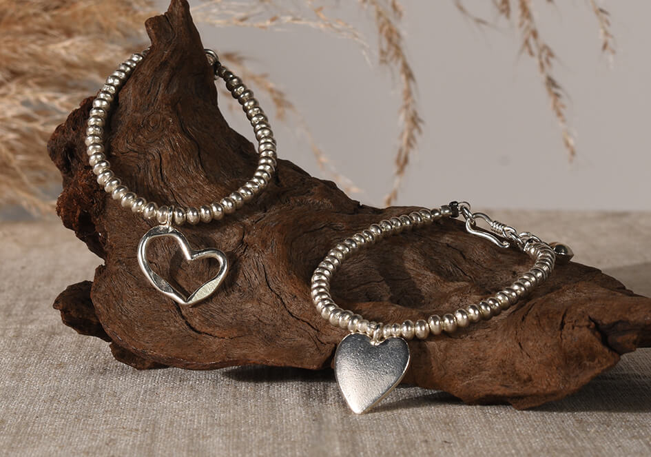 Two cherished heart beaded bracelets with cut-out heart and heart plate charm placed on top of wooden prop with pampas grass as backdrop.