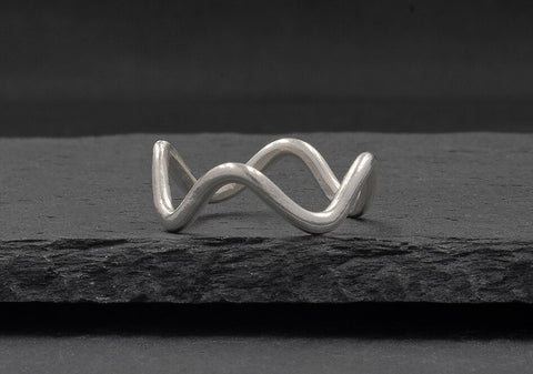 Minimalist wave ring from Hill to Street seating on a dark grey stone over black background